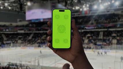 GREEN SCREEN CHROMA KEY A hand holding a phone with a green screen at a hockey game in an indoor stadium, ideal for showcasing live sports or betting apps
