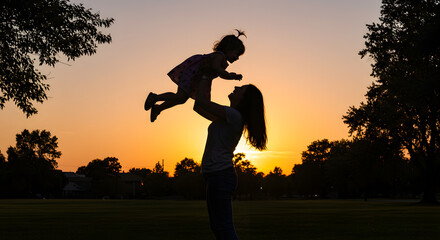 Fototapeta premium Mother lifting baby girl sunset silhouette
