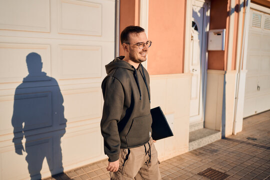 Smiling technician walking with laptop in residential area
