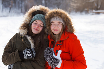 Two girls in winter, in warm clothes, enjoying the snow, outdoor. Cold time of the year, laughter and fun. Winter forest, white glade.