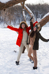 Two girls in winter, in warm clothes, enjoying the snow, outdoor. Cold time of the year, laughter and fun. Winter forest, white glade.