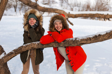 Two girls in winter, in warm clothes, enjoying the snow, outdoor. Cold time of the year, laughter and fun. Winter forest, white glade.