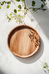 A minimalist wooden plate with soft natural lighting, surrounded by delicate green branches casting shadows on a white surface, creating a serene, organic atmosphere.

