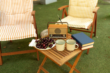 The FM channel is playing music, a stylish Vintage radio player stands on a wooden table. Cozy interior courtyard with sun loungers, on table cups, books, Retro FM radio player in Garden for leisure. 
