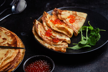 Pancakes with red caviar in a black plate close-up on the table. 