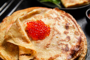Pancakes with red caviar in a black plate close-up on the table. 