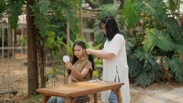 Asian mother braids her daughter's hair