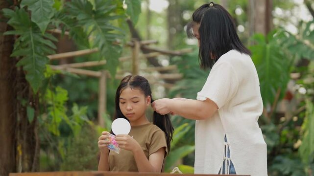 Asian mother braids her daughter's hair