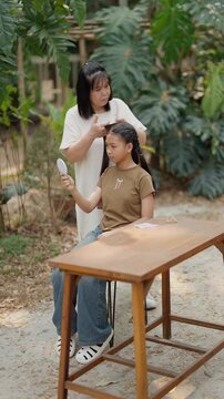 Asian mother braids her daughter's hair