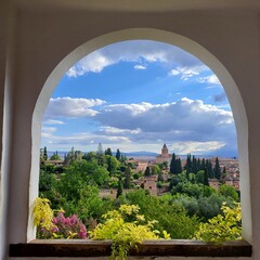 A view through a white archway frames the Alhambra palace and gardens in Granada, Spain, under a...