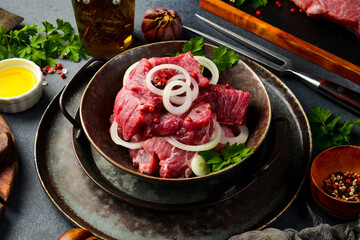 Raw pork neck cut into cubes in a bowl with onions and spices. Marinating kebab. On a gray stone background.