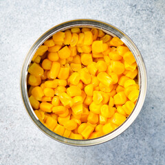 Pickled yellow sweet corn in a metal jar. Food stocks. On a gray concrete background.