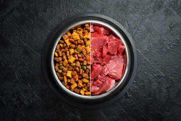 Bowl with food for dogs or cats. Fresh beef and dry fodder. On a black stone background.