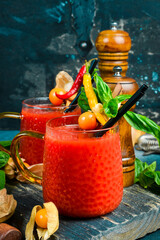 Glass of tomato alcoholic cocktail with spices and basil. On a dark stone table.
