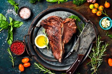 Steak on the bone. Grilled T-bone steak with rosemary and spices on a metal plate. Top view.