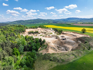 Aerial drone view of sand or gravel quarry surrounded by forest and farmland with distant hills. Aerial Drone view shows an inactive or abandoned quarry embedded in a green landscape.