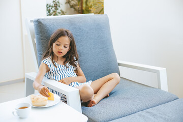 Young girl sitting comfortably on a cushioned chair, sipping a hot drink from a white cup
