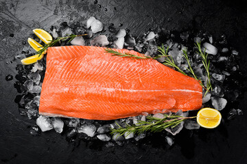 Fresh salmon fillet with rosemary and lemon on ice. On a stone background. Top view.