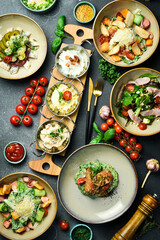 A set of food and dishes in plates. Top view. Food banner. On a dark stone background.