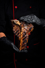 Steak on the bone in the hands of the chef. Prime Black Angus T-Bone Steak. Close-up. On a black...
