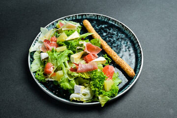 Fresh salad: prosciutto, brie cheese and pineapple. On a dark background, close-up.