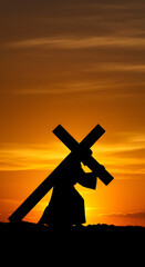 Silhouette of Person Carrying Cross Against Golden Sunset Sky