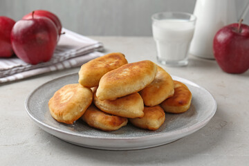 Delicious fried pyrizhky (stuffed pies), apples and milk on light grey table, closeup