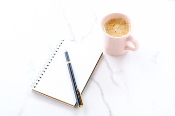 コーヒーを飲みながら、リング式のメモ帳とペンでデスクワークをしているイメージ
