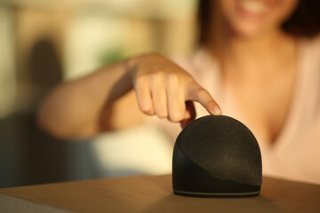 Happy woman turning on smart speaker with finger at home