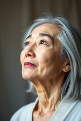 Fototapeta premium Close-up portrait of an elegant Asian woman with silver hair looking upward with gentle expression.