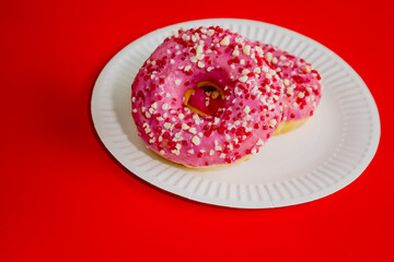 Donuts with pink glaze on a white disposable plate against a red background.