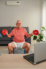 Smiling Senior man lifting weights at home following online fitness class on laptop