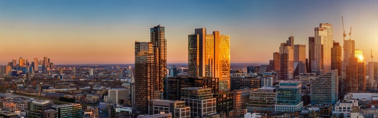 Panoramic sunset view of the skyline of London, from Canary Wharf over Shoreditch until the City with soft sunset light reflections in the glass facades of the modern skyscrapers