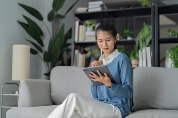 Asian woman using tablet writing ideas and memo at her home