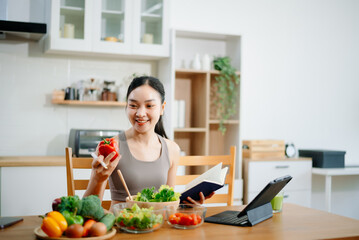 Female athete in sportswear standing in kitchen in sportswear and writing down healthy recipe. Active healthy lifestyle, clean eating