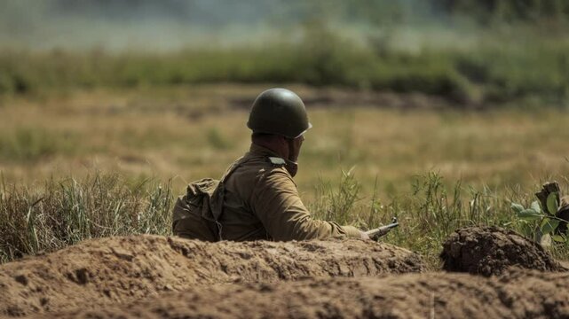 Aged Red Army infantryman sits down in trench and prepares for defense during Great Patriotic War in USSR historical reconstruction. Soviet soldier at combat simulation. WWII recreation battle. Summer