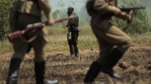 Soviet forces are in trench during World War 2 battle simulation. Red Army soldier transporting heavy Maxim machine gun across grassy battlefield. Great Patriotic War military history reconstruction