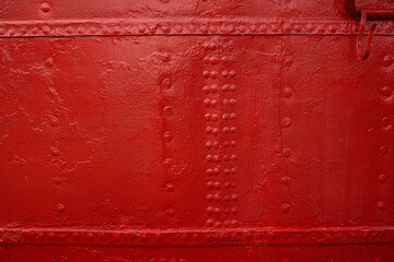 A closeup view of an industrial red painted metal surface with symmetrical rows of rivets,...