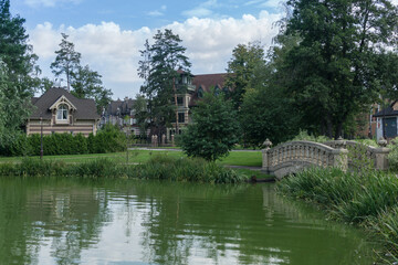 Fototapeta premium Idyllic landscape with a bridge over a stream on a summer day. Private territory of an .elite village with beautiful houses.