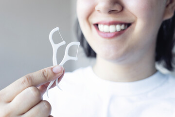 A young woman smiling and holding dental floss. Dental healthcare and orthodontic concept