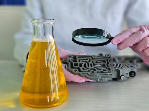 Engineer from flask yellow liquid into automatic transmission in chemical laboratory closeup. Testing lubricants for automotive parts