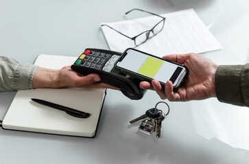 Hands using pos terminal  and smart phone to complete nfc payment during real estate  financinal...