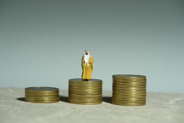 Miniature people toy figure photography. A King Sultan standing above gold coin money stack pile