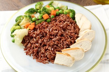 Delicious brown rice with chicken and vegetables served on wooden table, closeup