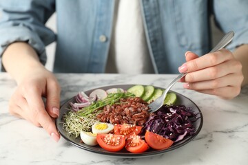 Woman eating delicious salad with brown rice at white marble table, closeup