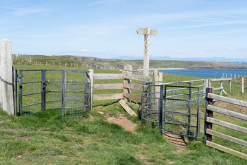 Kissing gates at a public footpath junction on a coast path with green fields and the sea in the distance.