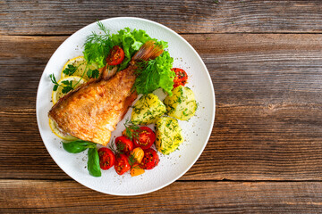 Fried atlantic redfish with boiled potatoes and tomato salad on wooden table