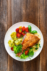 Fried atlantic redfish with boiled potatoes and tomato salad on wooden table