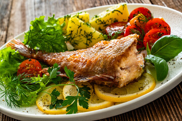 Fried atlantic redfish with boiled potatoes and tomato salad on wooden table