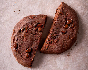 Top view of a broken chocolate cookie with visible chips on a beige stone surface. Horizontal layout, clean style, ideal for web design, packaging, ads, or food blogs.